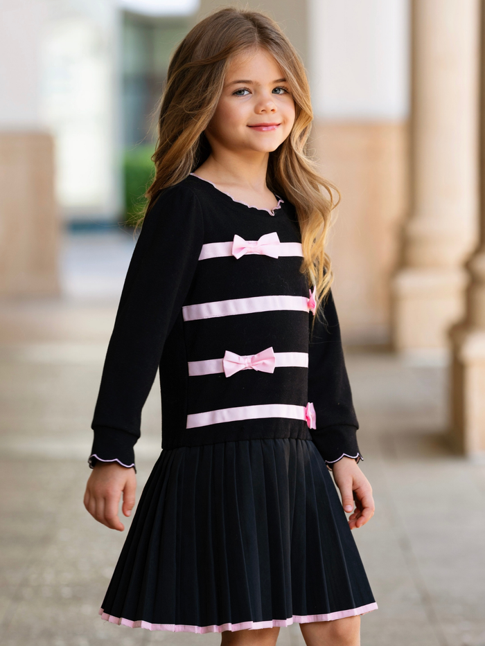 Girl wearing a black dress with pink satin bows and a pleated skirt for fall and holiday special occasions.