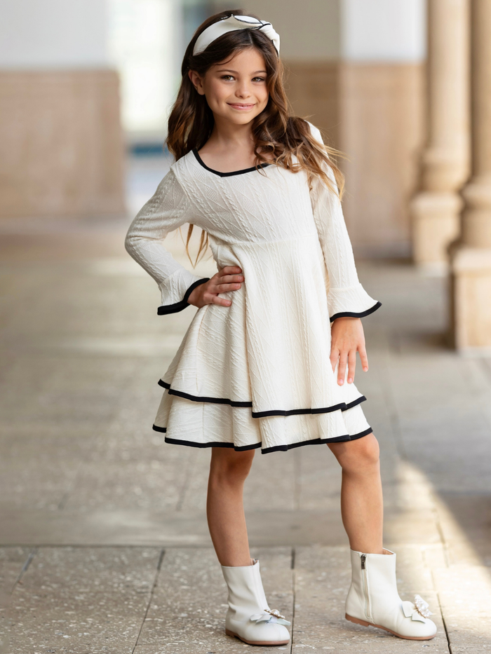 Girl wearing an ivory textured knit dress with black contrast trim for family photos and special occasions.
